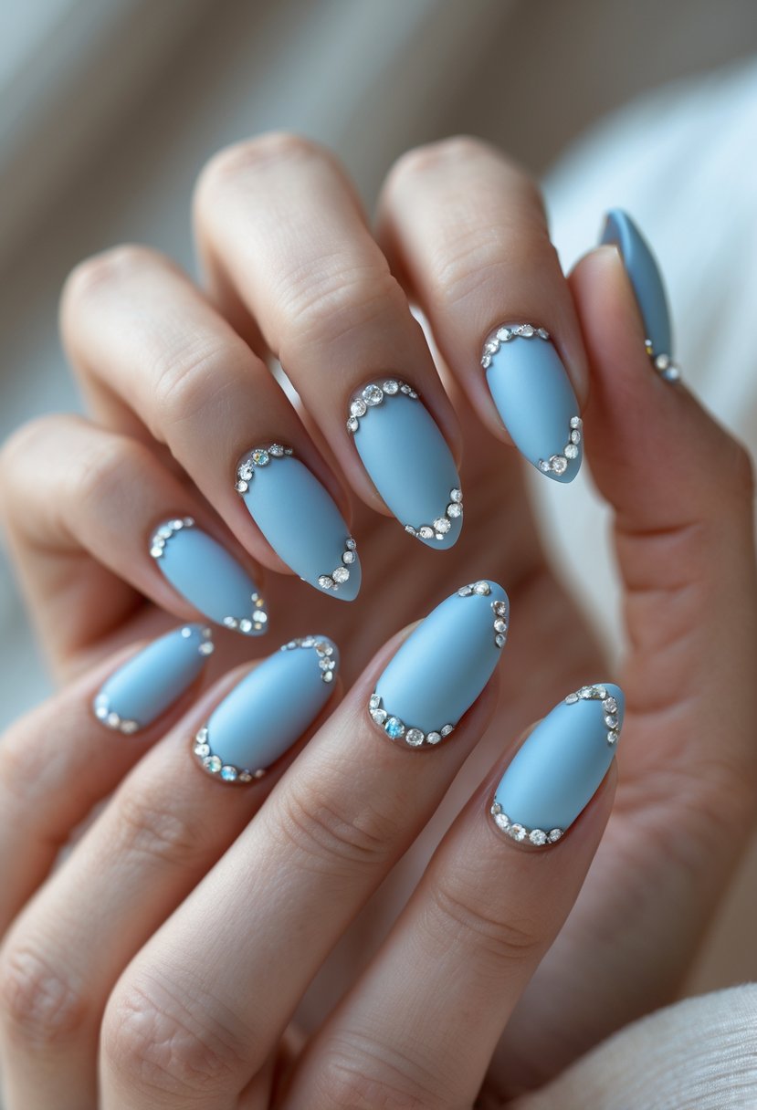 Close-up of a hand with short nails painted baby blue matte and decorated with small rhinestones.